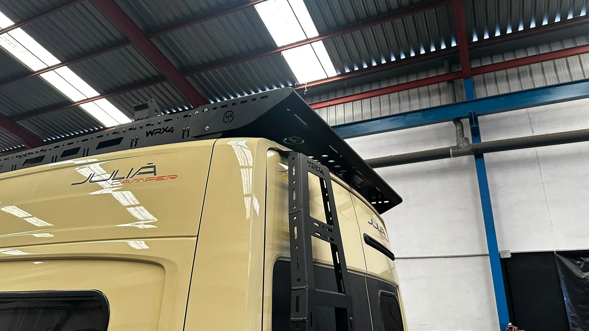 Escalera trasera WRX4 en la puerta de una camper MAN beige, bajo la visera trasera